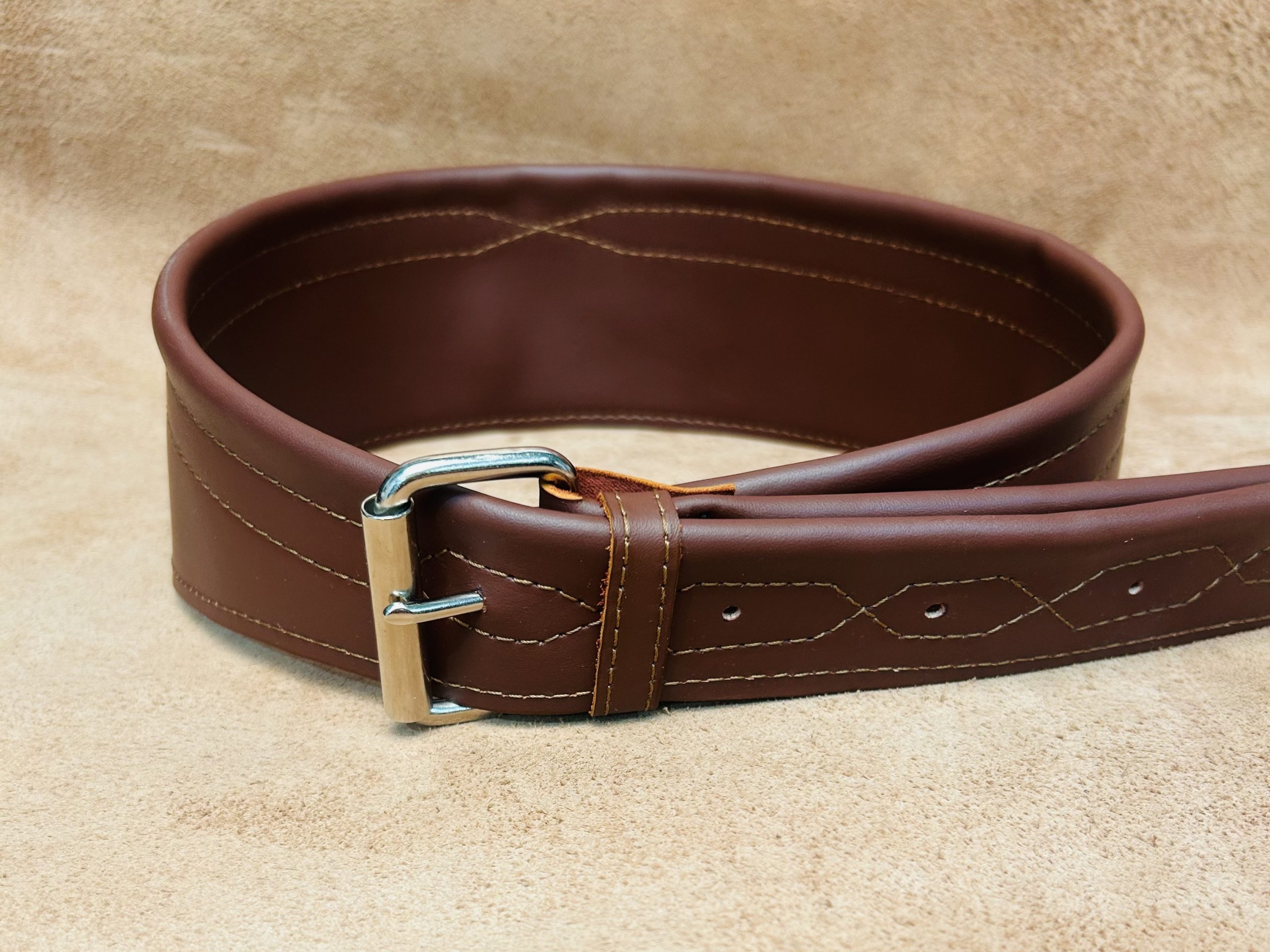 Guitar strap in leather color Cinnamon, rolled up on its side. The strap bas a large plain silver buckle